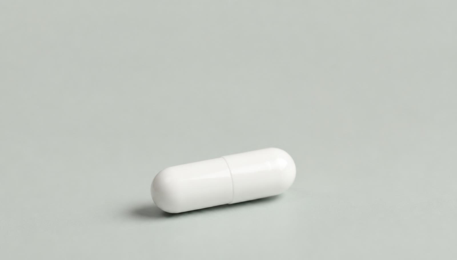 A single plain white capsule photographed on a pale seamless surface
